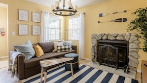 A cozy living room with a fireplace, a sofa with cushions, a coffee table, and a striped rug.