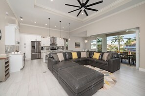 A spacious living area with a large sectional sofa, a kitchen with modern appliances, and a view of the outdoors through large windows.