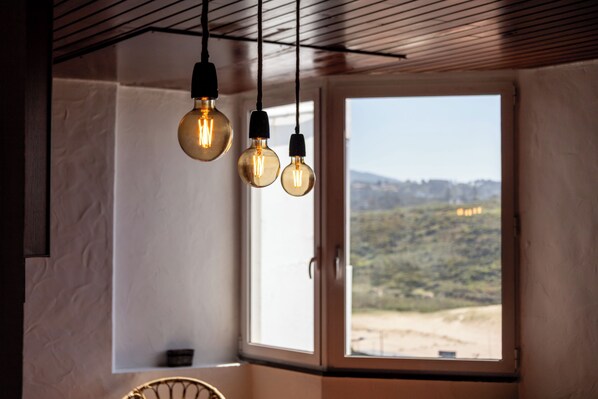 A room with a large window, a ceiling with wooden slats, and hanging light fixtures.