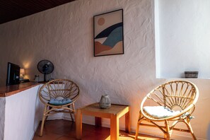 A room with two wicker chairs, a small wooden table, a wall-mounted fan, and a framed abstract painting. - Muito Acolhedor com Vista de mar (Colares)