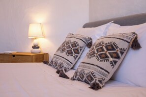 Ein Bett mit zwei dekorativen Kissen und einer Nachttischlampe auf einem Holznachttisch.