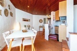 A modern kitchen with a built-in microwave, wooden cabinets, and a dining area with a white table and chairs. - Muito Acolhedor com Vista de mar (Colares)