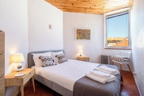 A bedroom with a bed, bedside tables, a lamp, a chair, a radiator, and a window with a view.