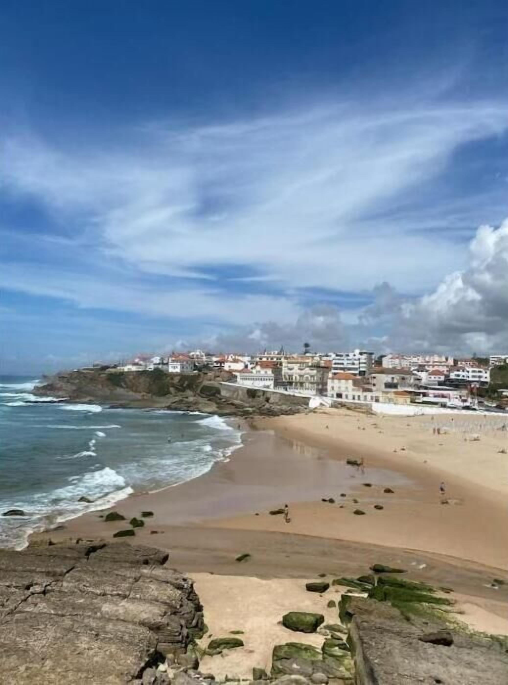 A coastal town with buildings along the beach, rocky shoreline, and waves crashing onto the shore.