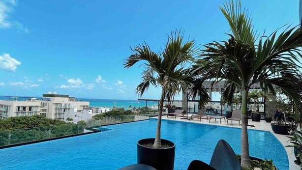 A modern pool area with a clear view of the ocean, surrounded by palm trees and contemporary lounge chairs.