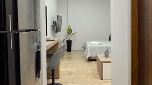 A modern hotel room with a kitchenette, a bed, a desk, and a chair.