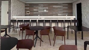 A modern restaurant with a long counter and multiple tables and chairs.