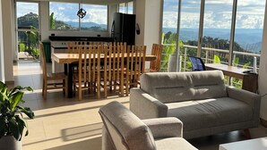 Un salon moderne avec un grand canapé gris, un coin repas avec une table et des chaises en bois, et une cuisine avec un réfrigérateur noir.