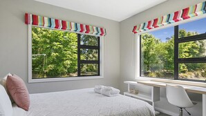 A bedroom with a bed, a desk, and large windows with curtains.