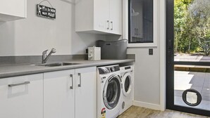 A modern laundry room with a washing machine, a sink, and a sign that reads "M is for MUM NOT MAID!".