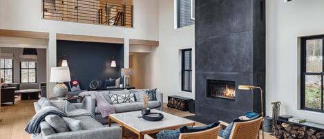 A spacious living area with a high ceiling, a fireplace, and a large window.