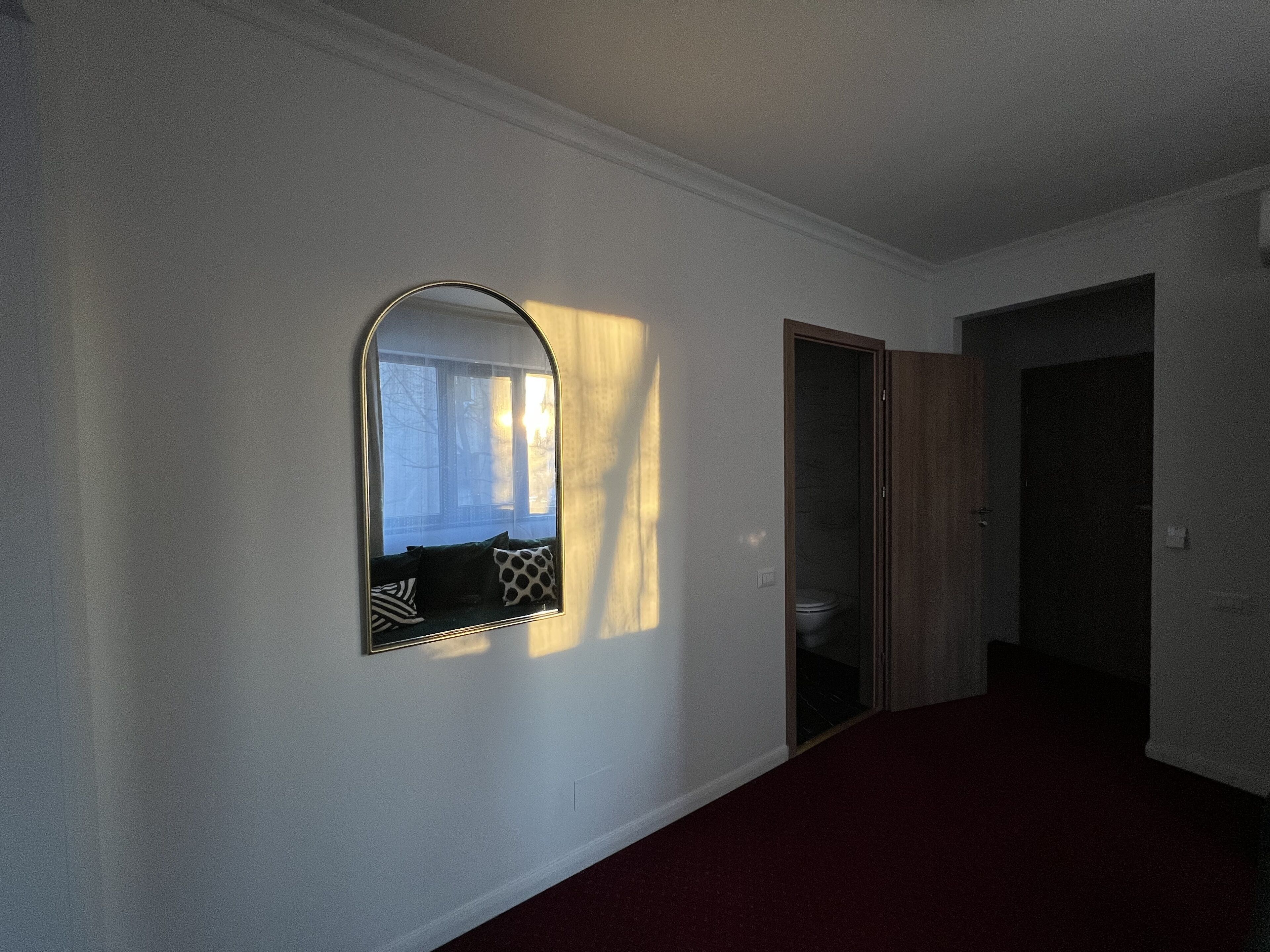 Un pasillo con un espejo, una puerta y vistas a una habitación con ventana.
