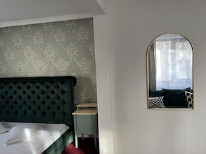 A bedroom with a tufted headboard, a bed with white linens, a green nightstand, a mirror, and a patterned wallpaper. - Eden Boutique Accommodation (Bucharest)