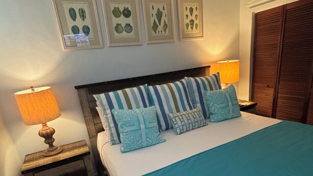 A bedroom with a bed, two bedside tables, a nightstand, a wooden wardrobe, and wall art.