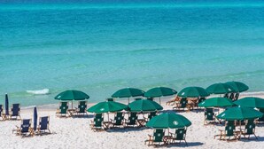 Una playa con hileras de sombrillas verdes y sillones de madera orientados al océano.