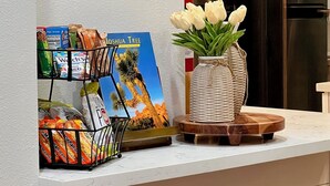 A kitchen counter with a snack rack, a book titled 'Joshua Tree', and a vase with white flowers. - Easton Flats- A Couples Retreat! (Twentynine Palms)