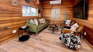 A cozy cabin interior with a wooden interior, a green sofa, a leather armchair, and a cowhide ottoman. - Easton Flats- A Couples Retreat! (Twentynine Palms)
