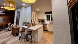 A modern kitchen with white cabinets, a stainless steel sink, and a wooden island with stools. - Easton Flats- A Couples Retreat! (Twentynine Palms)