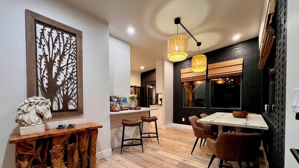 A modern kitchen with a dining area, featuring a wooden table and chairs, a decorative tree wall art, and a unique wooden console table. - Easton Flats- A Couples Retreat! (Twentynine Palms)