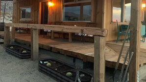 A wooden cabin with a porch, multiple windows, and a small garden area with cacti. - Easton Flats- A Couples Retreat! (Twentynine Palms)