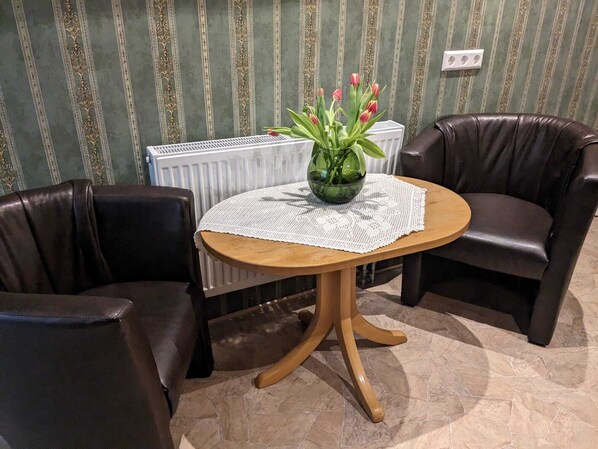 Een eethoek met een ronde tafel, twee lederen stoelen, een vaas met bloemen en een radiator op de achtergrond.