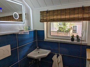 Een badkamer met een wastafel, spiegel en raam met zonwering.