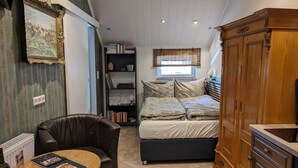 Et kompakt soveværelse med seng, siddeplads med bord, bogreol og skab.
