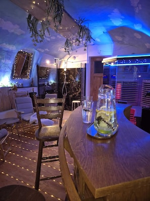 Ein gemütliches Zimmer mit einem Holztisch, Stühlen, einer Glasflasche mit einer Pflanze und einem Spiegel an der Wand.