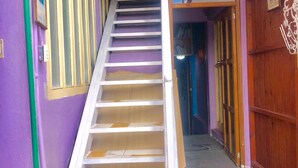 A staircase leading to a landing with a purple wall and a wooden door on the right. - Room-central Comfy Small Studio (San Cristóbal de las Casas)