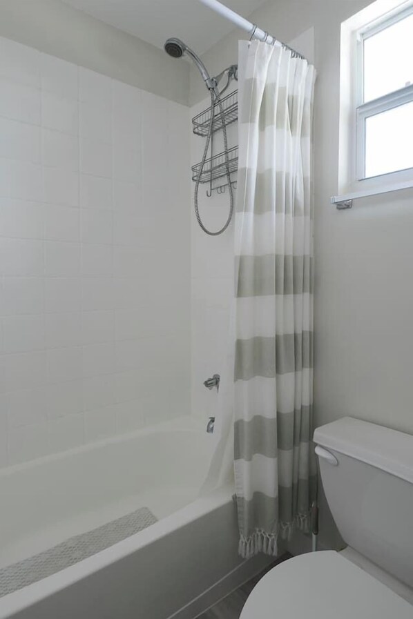 A bathroom with a shower, toilet, and a window.