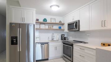 Una cocina moderna con armarios blancos, electrodomésticos de acero inoxidable y una repisa de madera con objetos decorativos.
