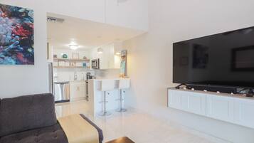 Una sala de estar moderna con un televisor de pantalla plana, un sofá, una mesa de centro y una cocina al fondo.