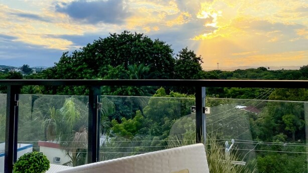 Un balcón con vista al atardecer, una silla blanca y una pequeña planta en maceta.