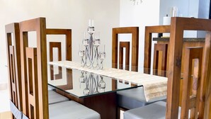 Un comedor con mesa de vidrio, sillas de madera con asientos acolchados y un reloj de pared.