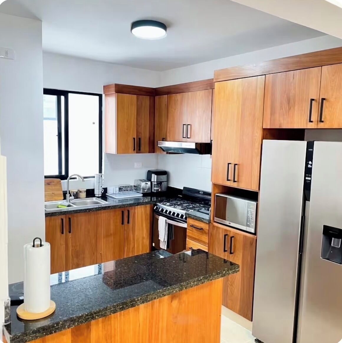 A kitchen with wooden cabinets, a stainless steel refrigerator, a gas stove, and a microwave.