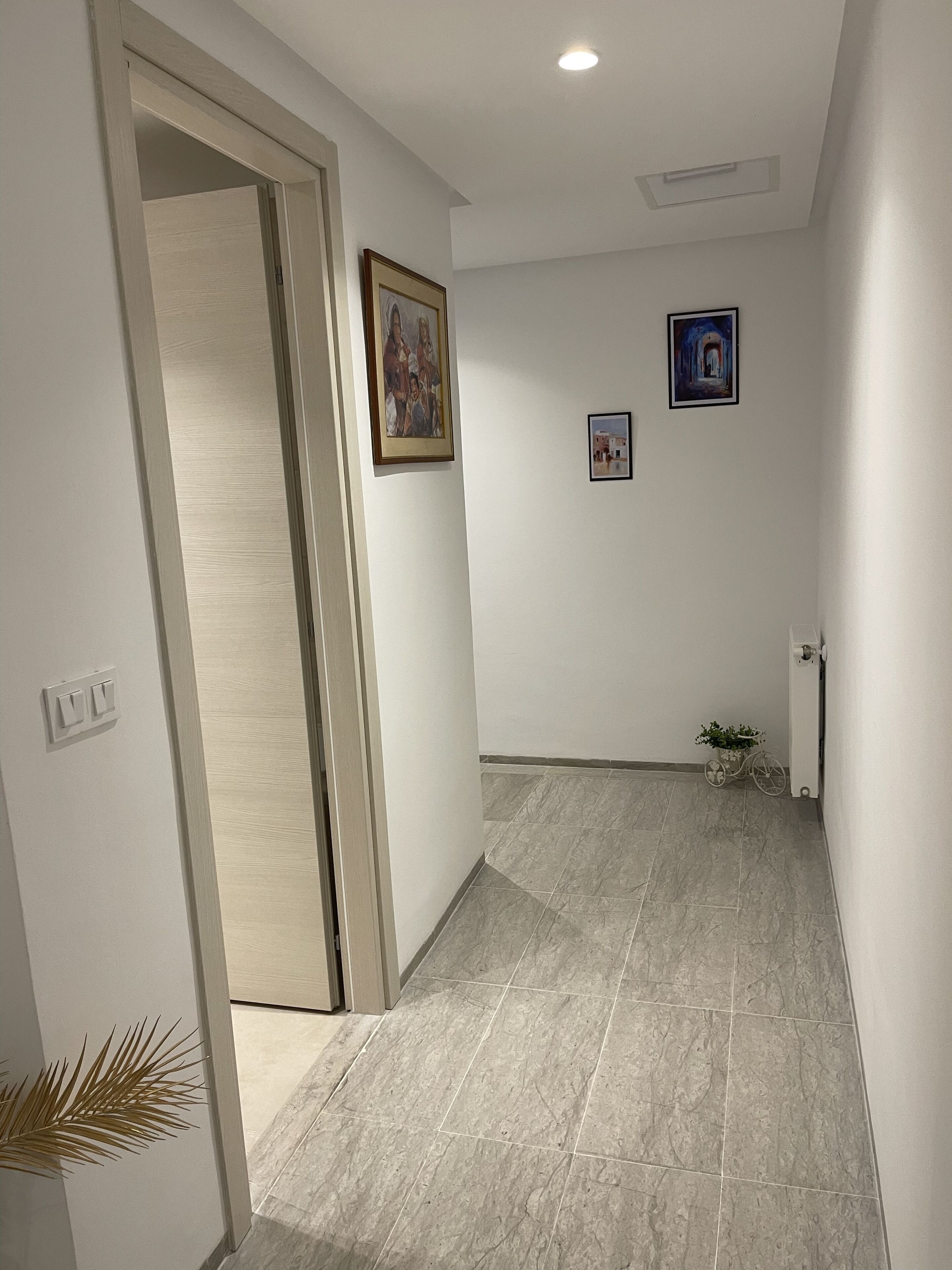 Un couloir avec un sol carrelé, une porte et deux tableaux encadrés accrochés au mur.