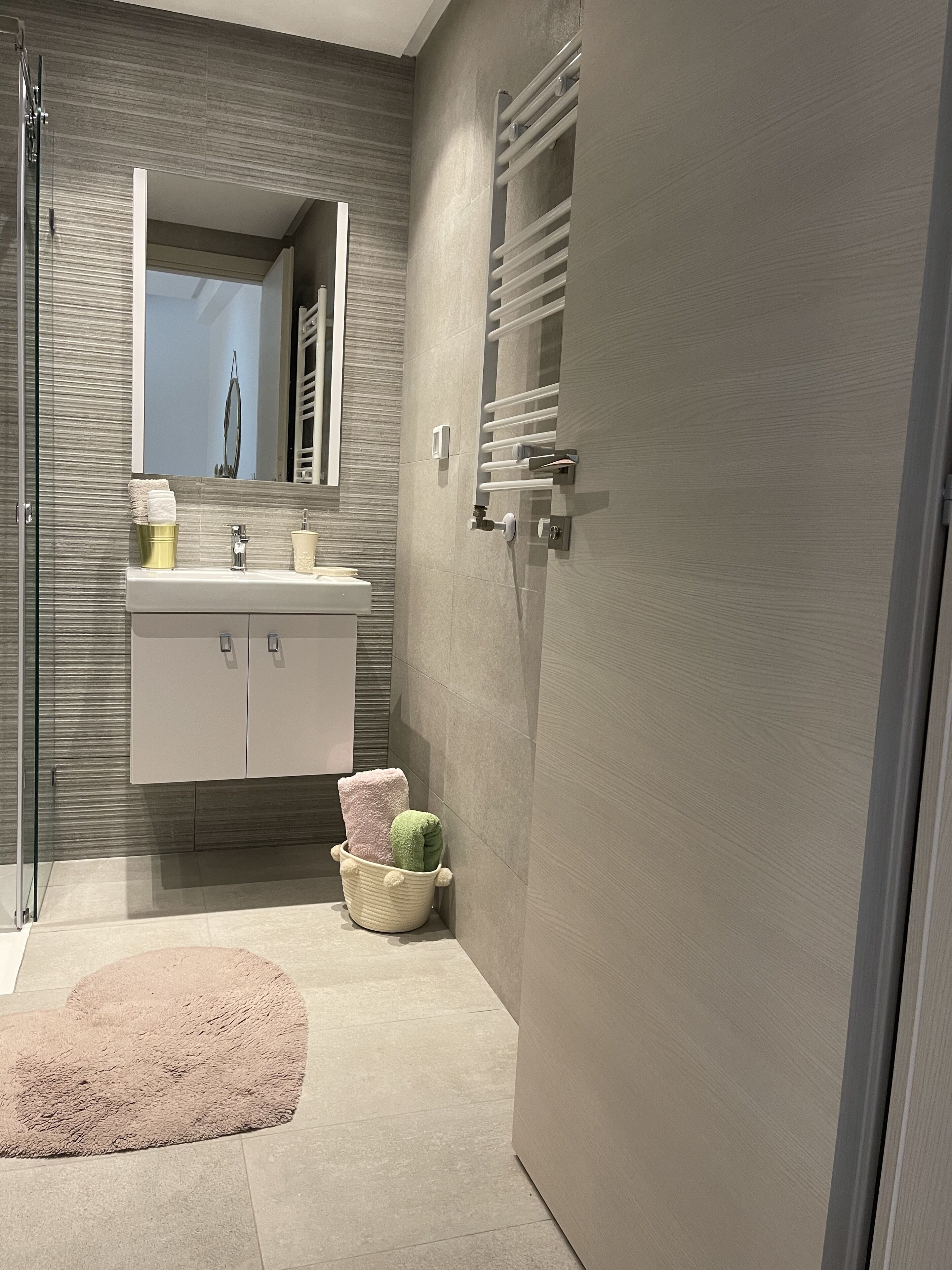 A modern bathroom with a glass shower enclosure, a white vanity with a mirror, and a towel rack.