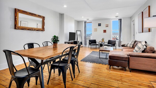 Una sala de estar moderna con una mesa de comedor de madera, sillas negras, un sofá de cuero marrón y un espejo grande en la pared.