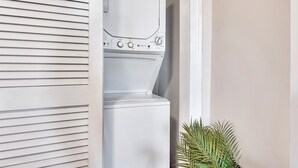 A front view of a white stacked washer and dryer unit with control knobs and a small plant beside it. - Uncle Sam's Hideaway |Nearby Colleges & Hospital|Personal Workspace|Pet Friendly (Troy)