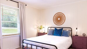 A bedroom with a bed, a nightstand, a wall decoration, and a window with curtains. - Artist's Bungalow- 1/2 mi from Covington Square (Covington)