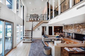 A spacious living area with a fireplace, a staircase, and a view through large windows.