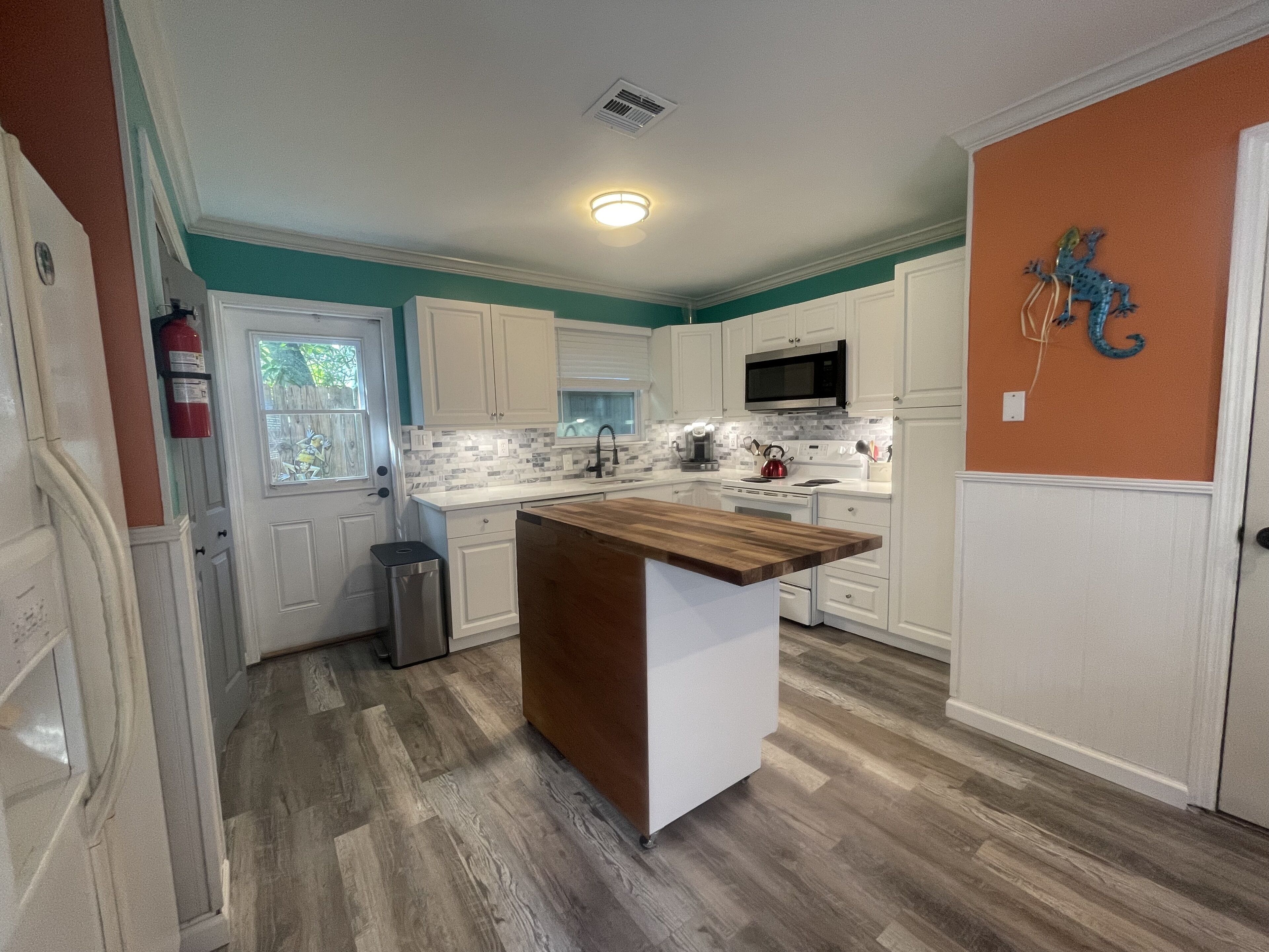 A modern kitchen with white cabinetry, a wooden island, and a tiled backsplash.