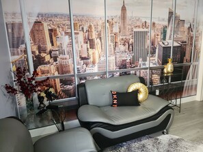 A modern living room with a sofa and a glass coffee table, a decorative vase with red flowers, and a large window with a cityscape view. - Mimi's Ste K2 Casino (Tampa)
