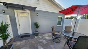 A patio with a glass table and chairs, a red umbrella, and potted plants.
