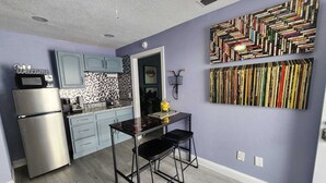 A modern kitchen with light blue cabinets, a stainless steel refrigerator, and a black dining table with two chairs.