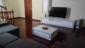 A living room with a flat-screen TV, a white entertainment unit, and a wooden staircase. - Casa sousa (Campanario)