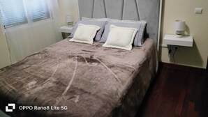 A bedroom with a bed, two bedside tables, and a window with blinds. - Casa sousa (Campanario)
