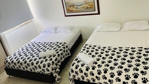 Hotellihuone, jossa on kaksi sänkyä. Kummassakin sängyssä on valkoiset vuodevaatteet ja musta tassunjälkikuviollinen kangas. Seinällä sänkyjen yläpuolella on kehystetty taulu.