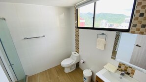 Kylpyhuone, jossa on wc, pesuallas ja lasiseinällinen suihkutila.