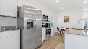 A modern kitchen with stainless steel appliances, white cabinetry, and a dining area with a table and chairs. - Dog Parks • Museums • Walking and Biking Trails (Centerton)